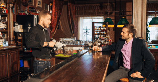 A man talking to a bartender at a bar